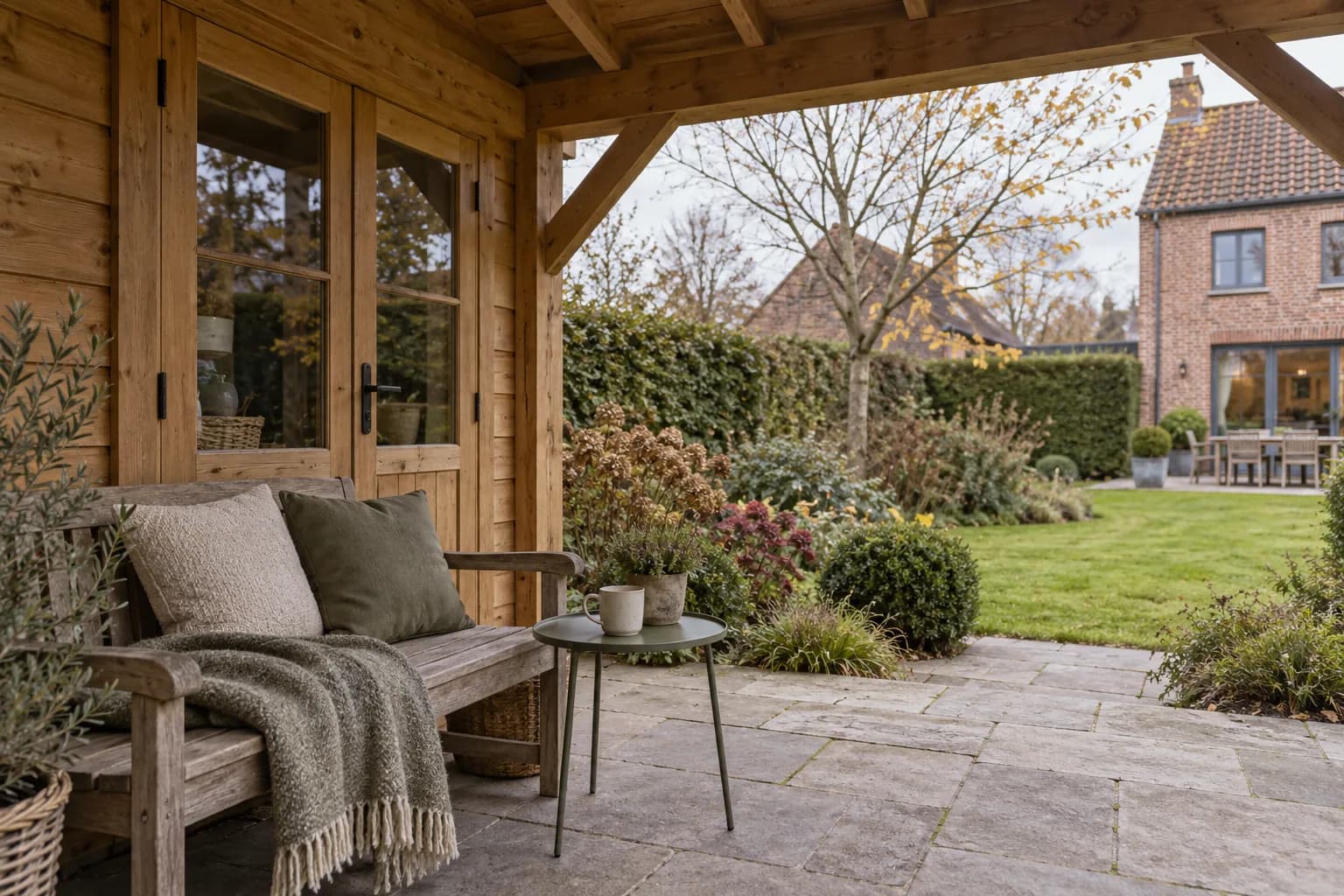 Banc avec coussins et petite table sous l’auvent en bois, face à la pelouse et à la maison