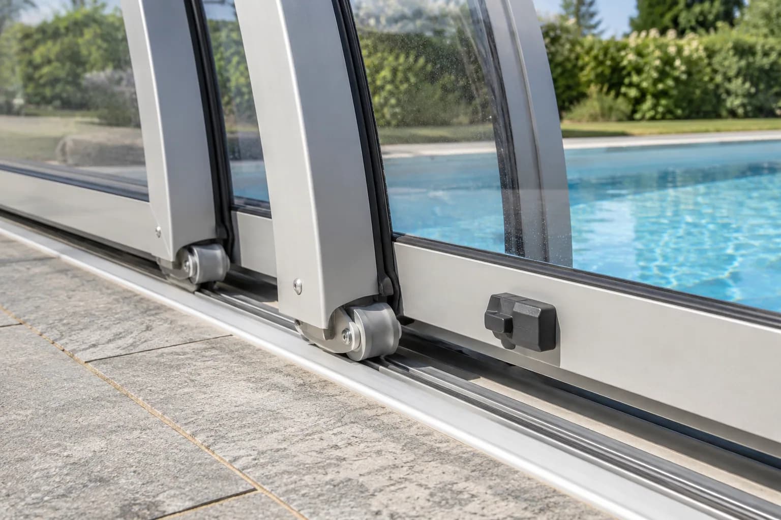 Roulettes et rail d'un abri de piscine, avec cadre aluminium, joint noir et verrou latéral.