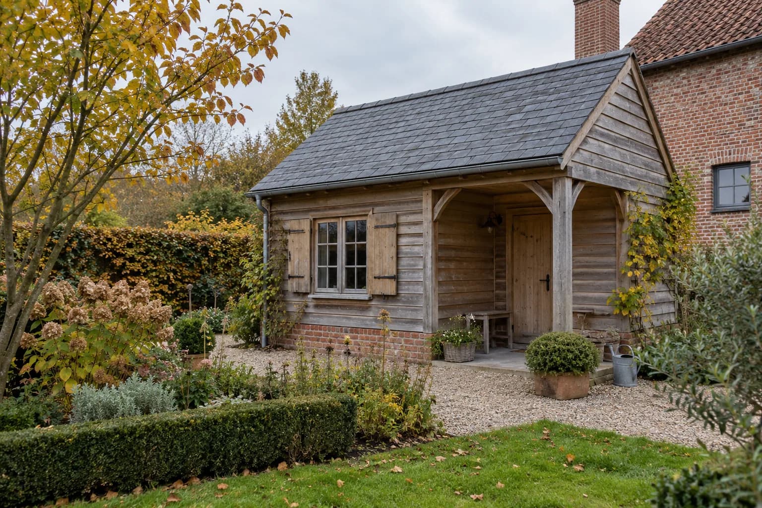 Annexe champêtre en bois patiné, toiture en ardoises, fenêtre à volets et petit porche.