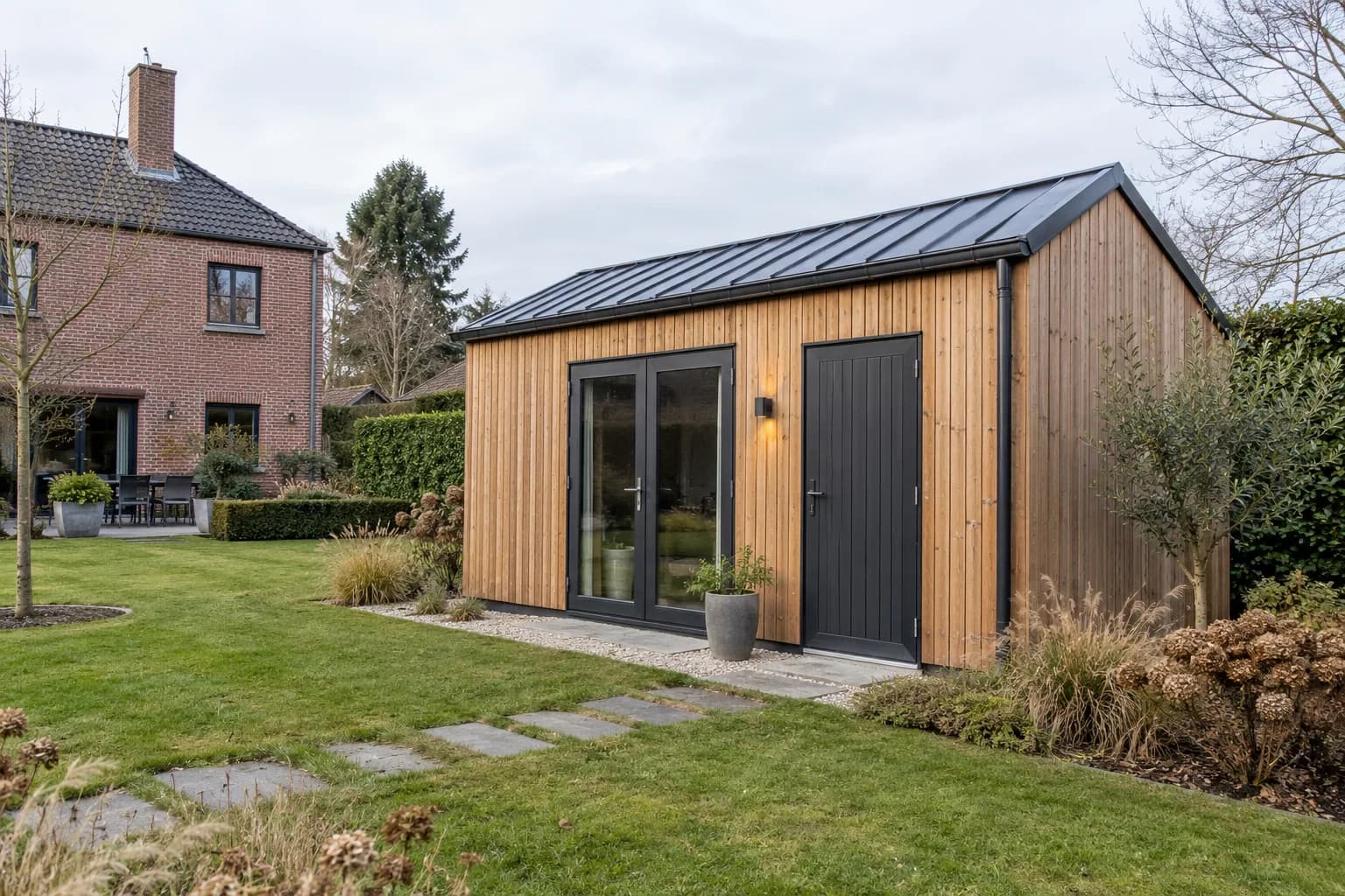 Annexe en bois à deux portes et toiture métallique dans le jardin d'une maison en brique.