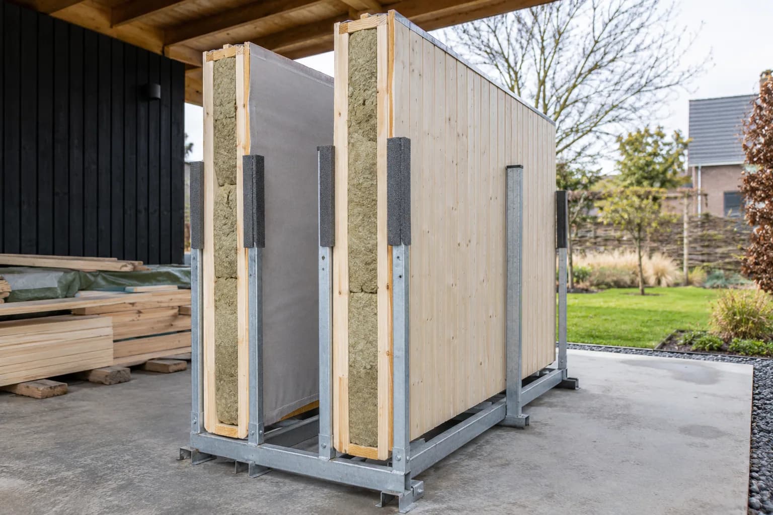 Deux panneaux de murs préfabriqués isolés, maintenus dans un rack métallique sous un abri de chantier.