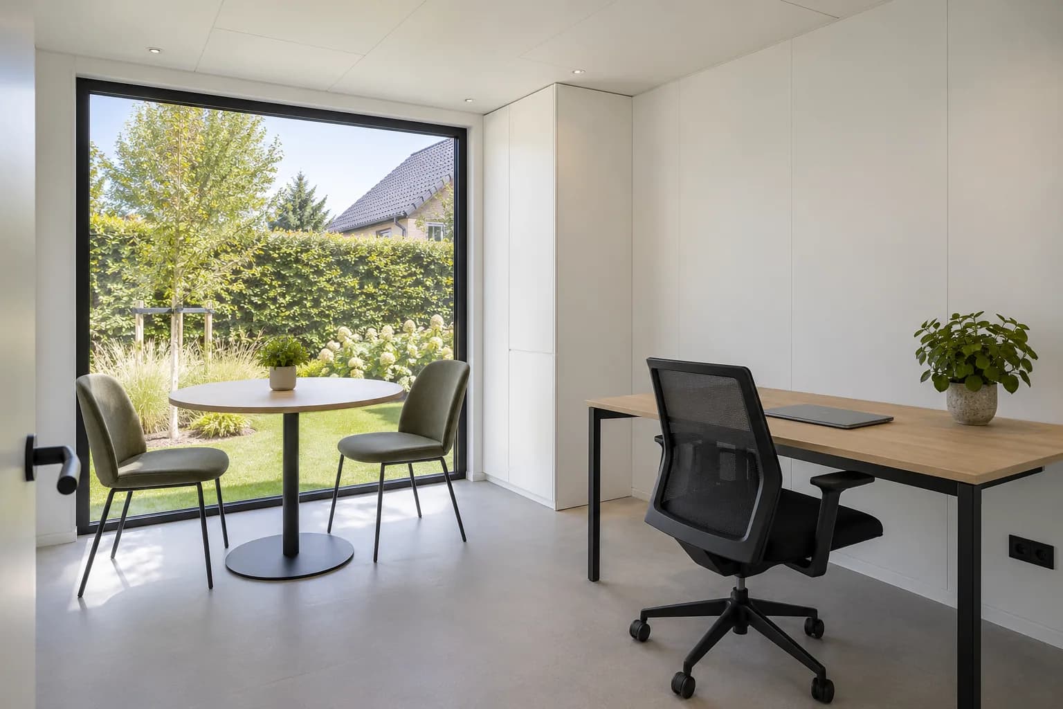 Bureau préfabriqué aménagé avec poste de travail et petite table de réunion devant une grande fenêtre.