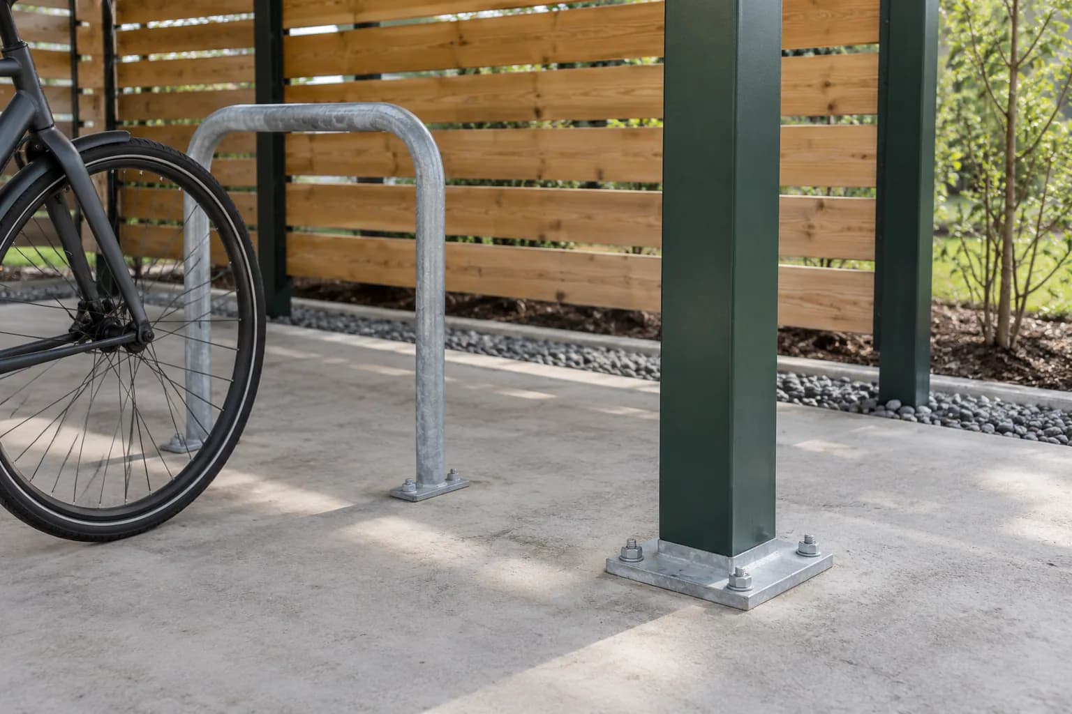 Platine de poteau boulonnée dans une dalle en béton, près d'un arceau de stationnement pour vélo.
