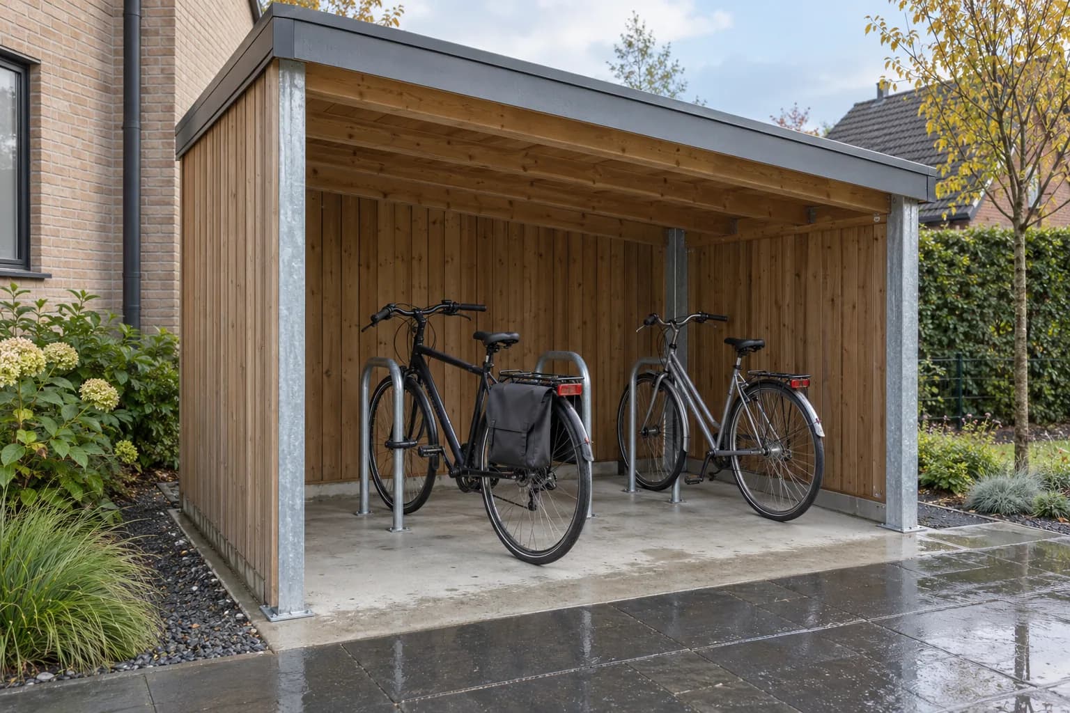 Deux vélos rangés sous un abri en bois et acier, avec une sacoche et un sol sec après la pluie.