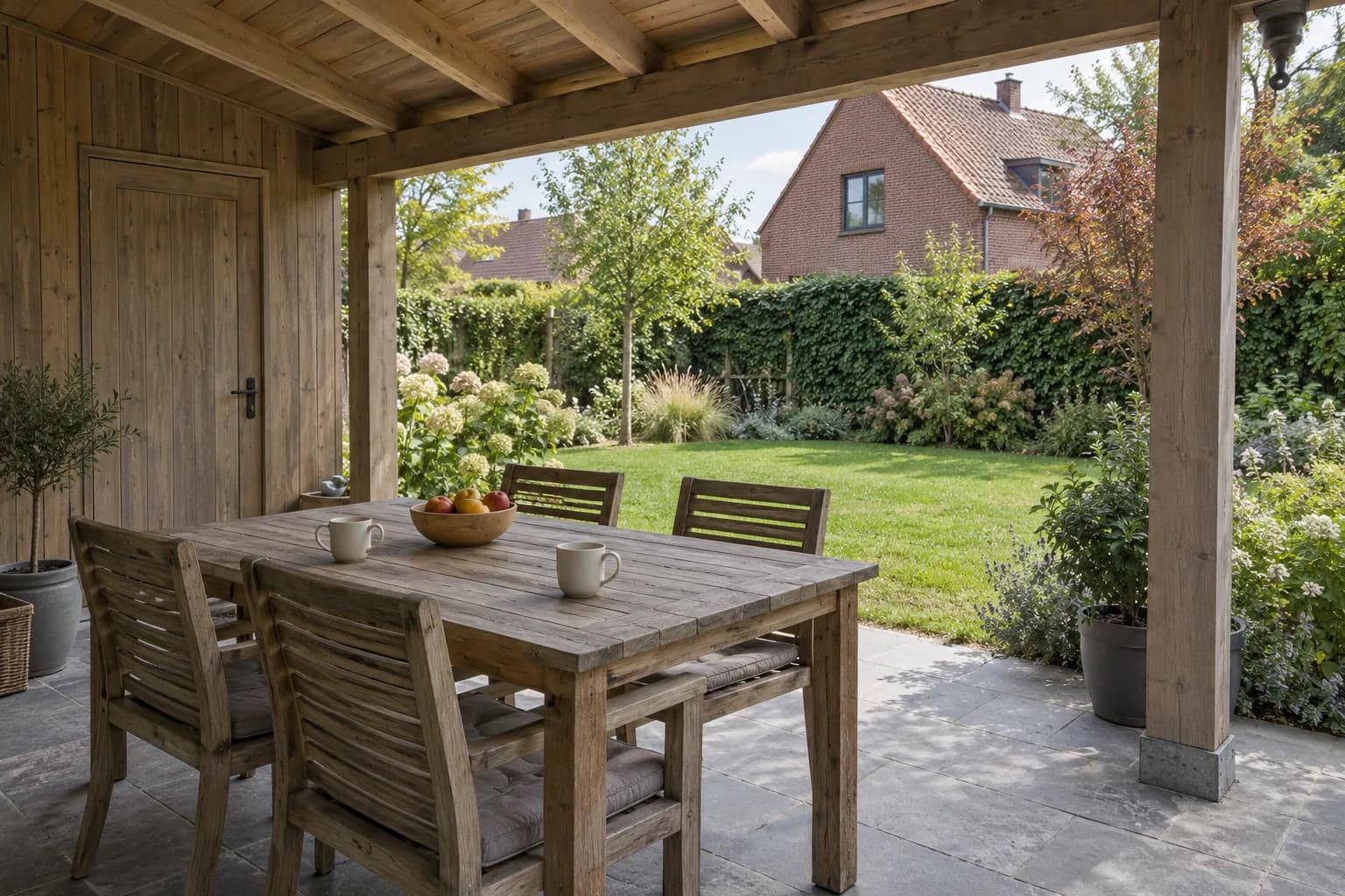 Table et chaises sous une annexe en bois ouverte sur le jardin et une maison en briques