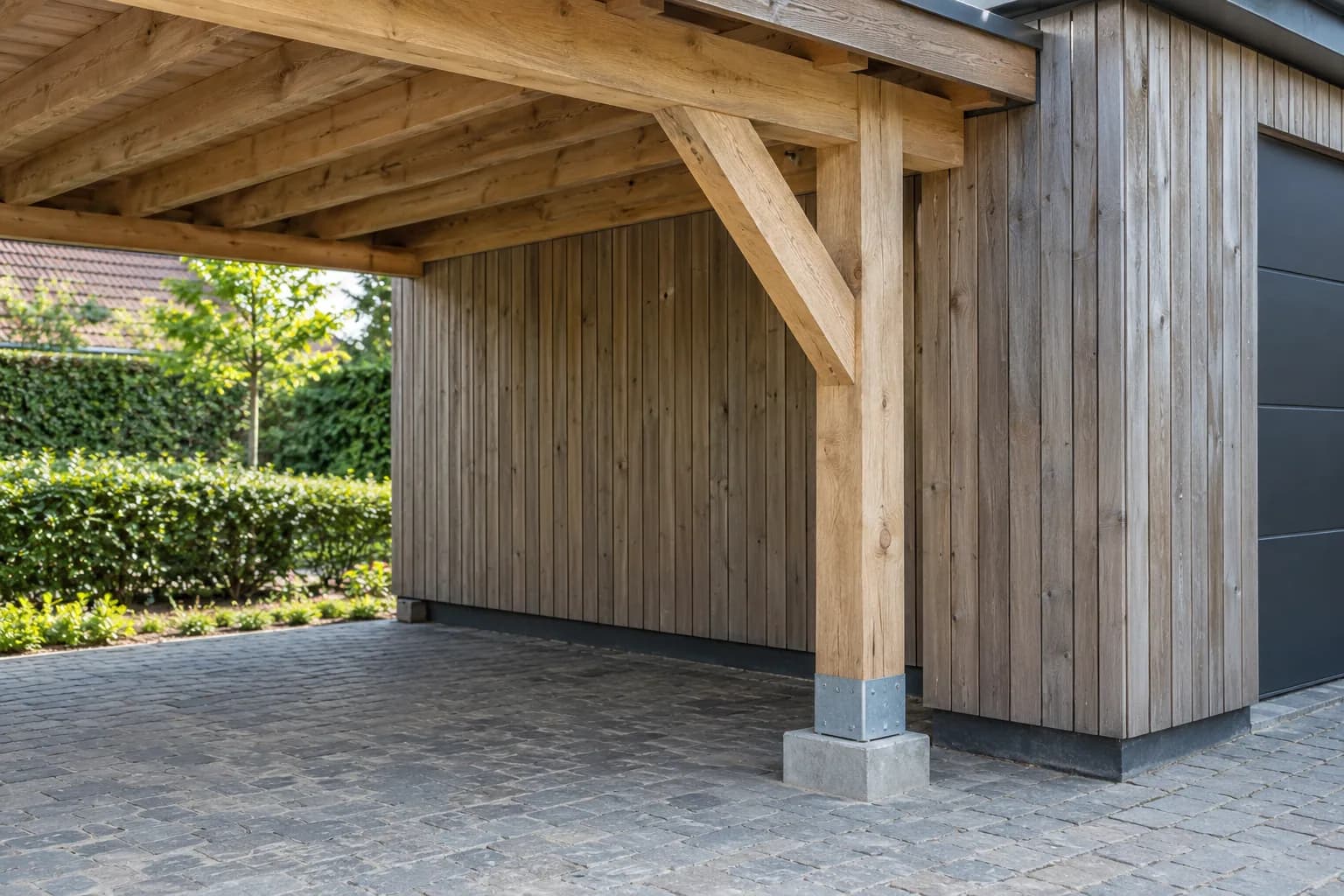 Poteau de carport en bois avec jambe de force, pied métallique et socle en béton près du garage.