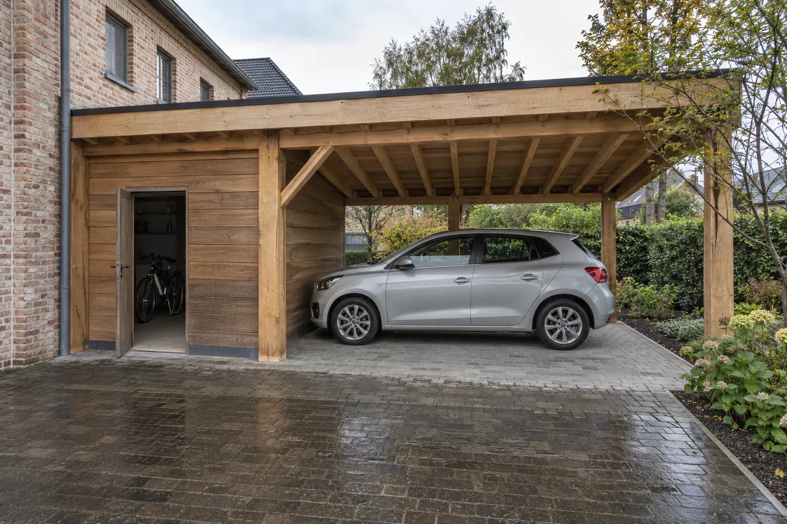 Voiture abritée sous un carport en bois, à côté d'une porte de service ouverte sur des vélos.