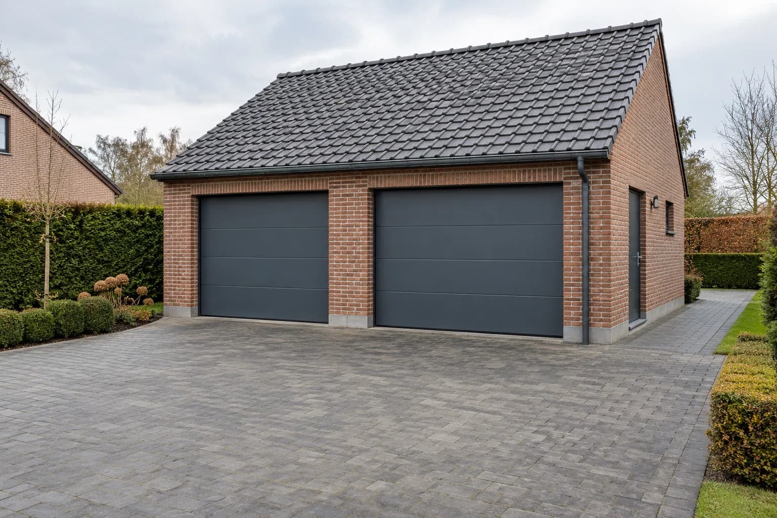 Garage double en briques avec deux portes sectionnelles anthracite et une large allée pavée.