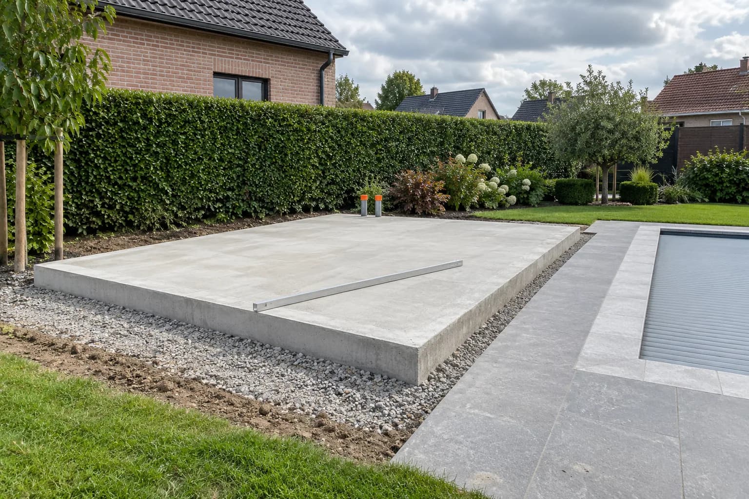 Dalle de béton destinée à un pool house, avec deux gaines bouchonnées et une règle posée près de la piscine fermée.