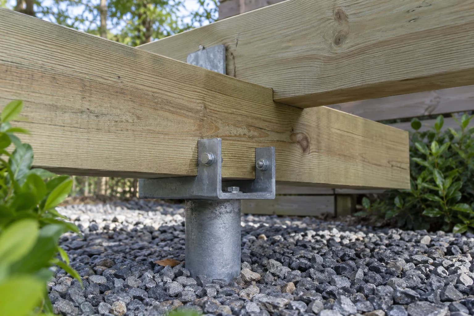 Poutre en bois fixée par boulons sur une tête métallique, avec espace libre au-dessus du gravier.