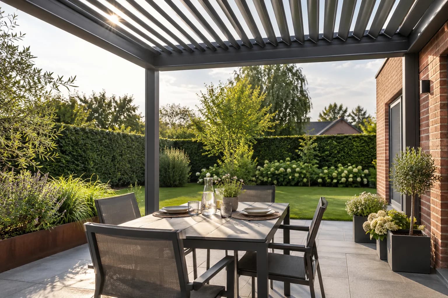 Table dressée sous une pergola à lames entrouvertes, avec vue sur la pelouse et les haies.