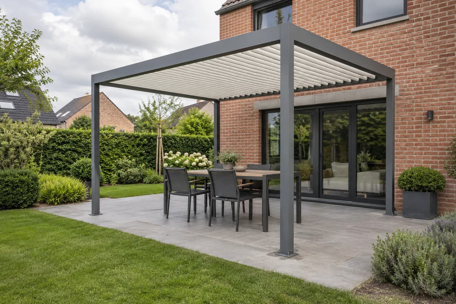 Pergola grise à lames claires au-dessus d'une table de jardin devant une maison en brique.