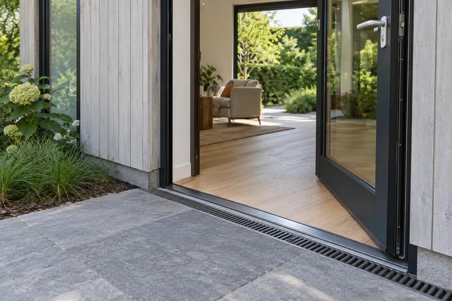 Entrée de plain-pied d'un logement de jardin avec seuil bas, porte vitrée et caniveau extérieur.