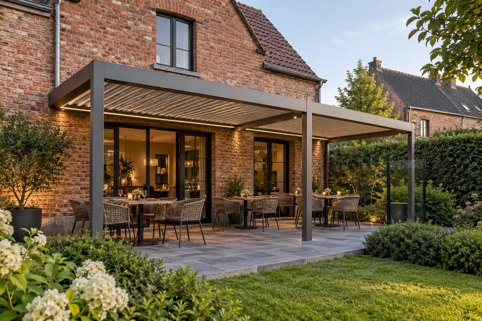 Terrasse de restaurant couverte par une structure grise à lames, avec plusieurs tables devant un bâtiment en briques.