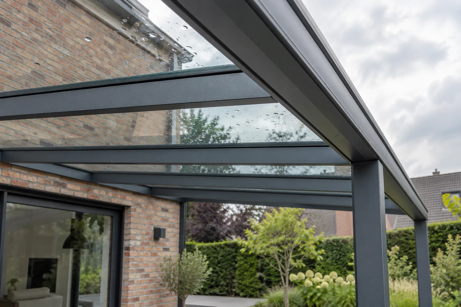 Gouttes de pluie sur le vitrage d’une toiture de terrasse soutenue par des profilés anthracite.