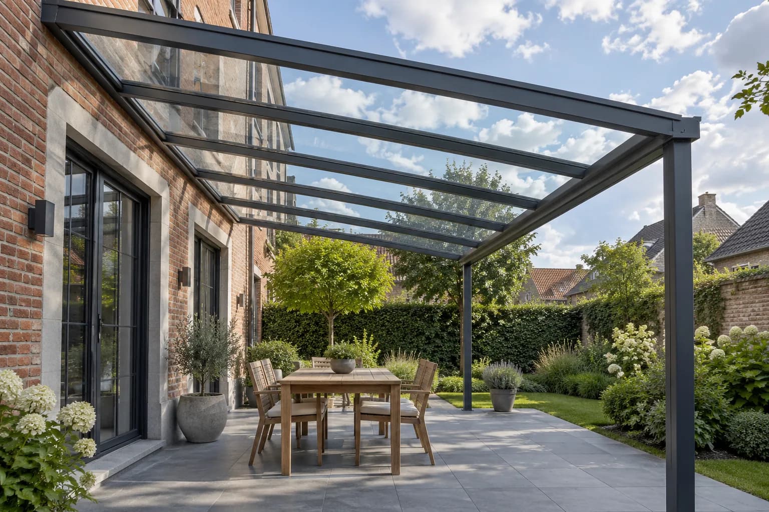 Toiture en verre transparent sur profilés anthracite au-dessus d’une terrasse avec une table en bois.