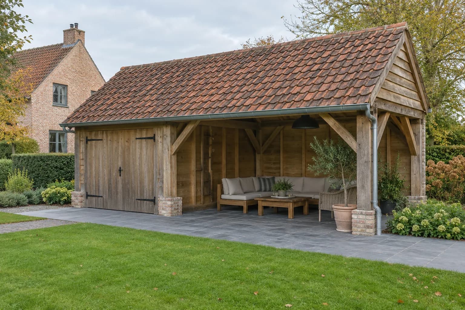 Houten bijgebouw met rood pannendak, gesloten berging en overdekte zithoek op een natuurstenen terras