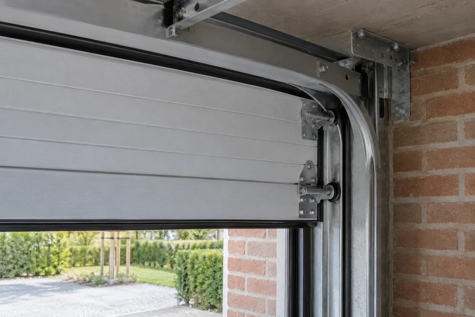 Metalen looprail, rollen en scharnieren van een gedeeltelijk geopende sectionaalpoort in een bakstenen garage.