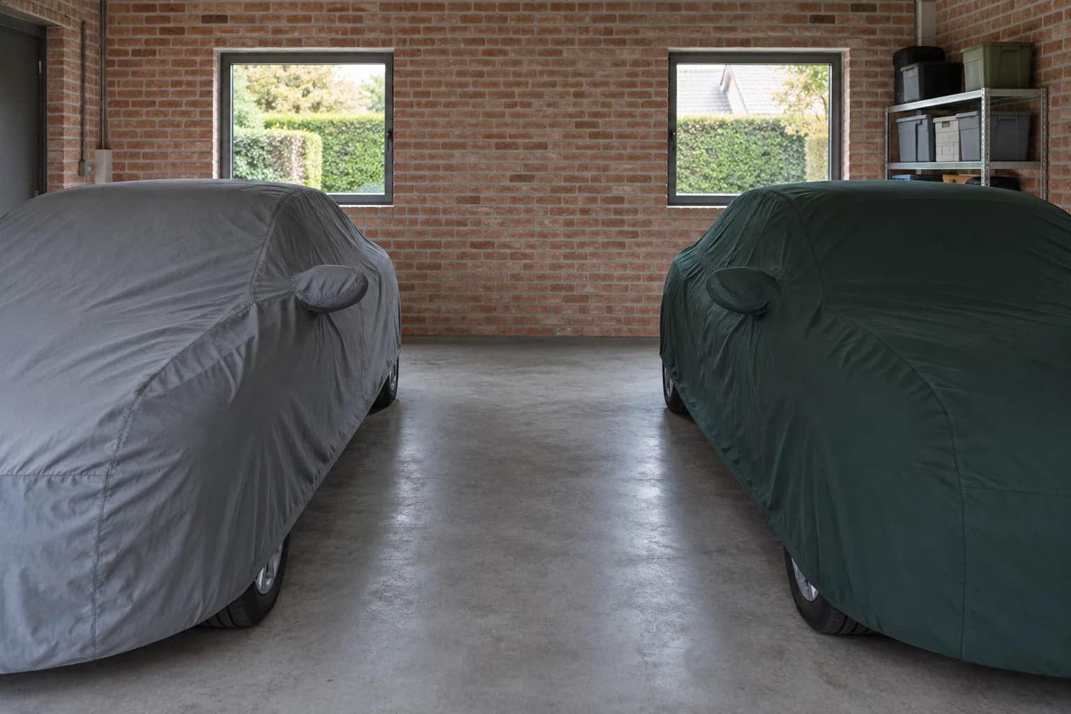 Twee auto's onder beschermhoezen in een dubbele garage met een vrije middenstrook en opbergstelling.