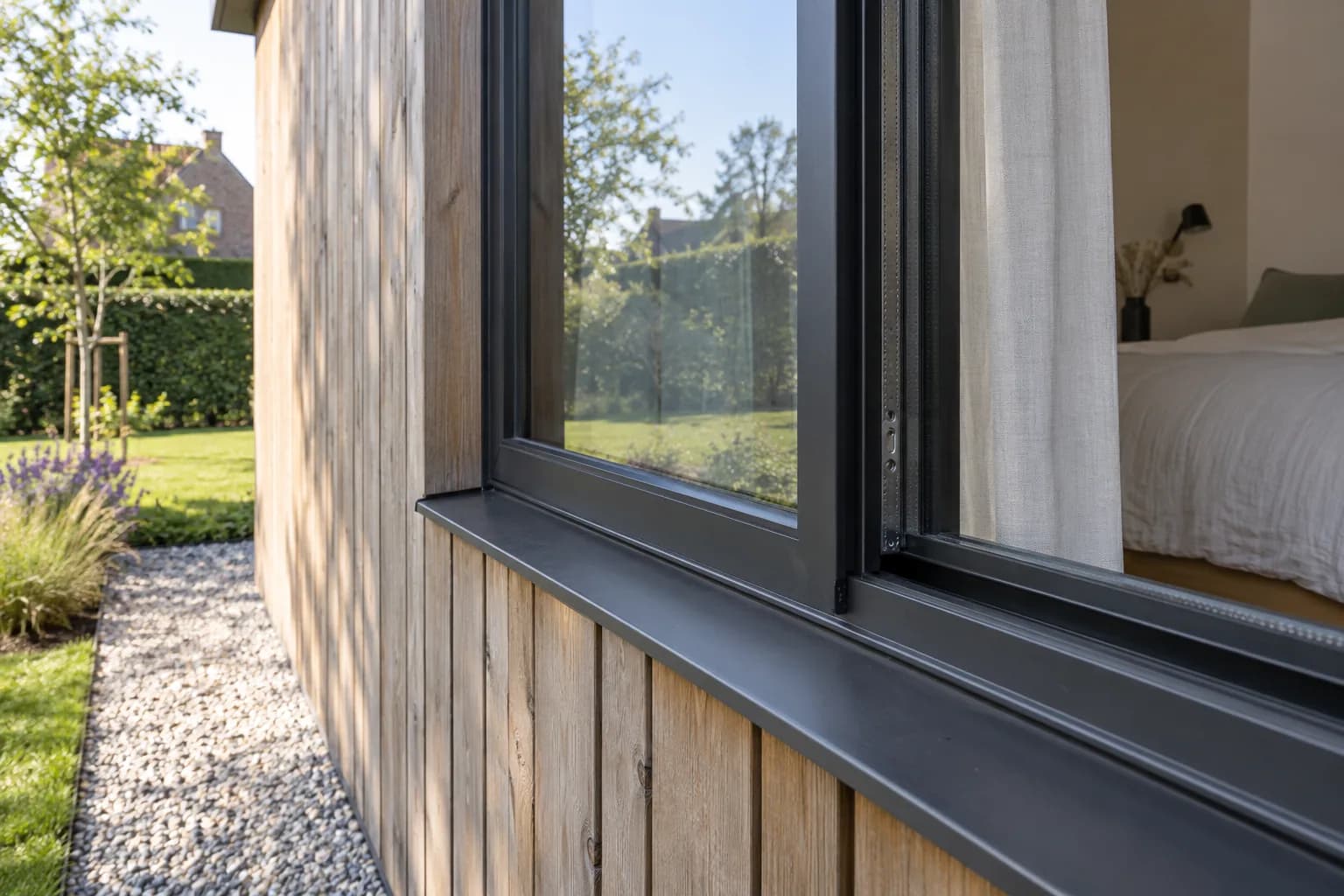 Donker raamprofiel met afdichting en metalen dorpel in de houten gevel van een gastenverblijf.