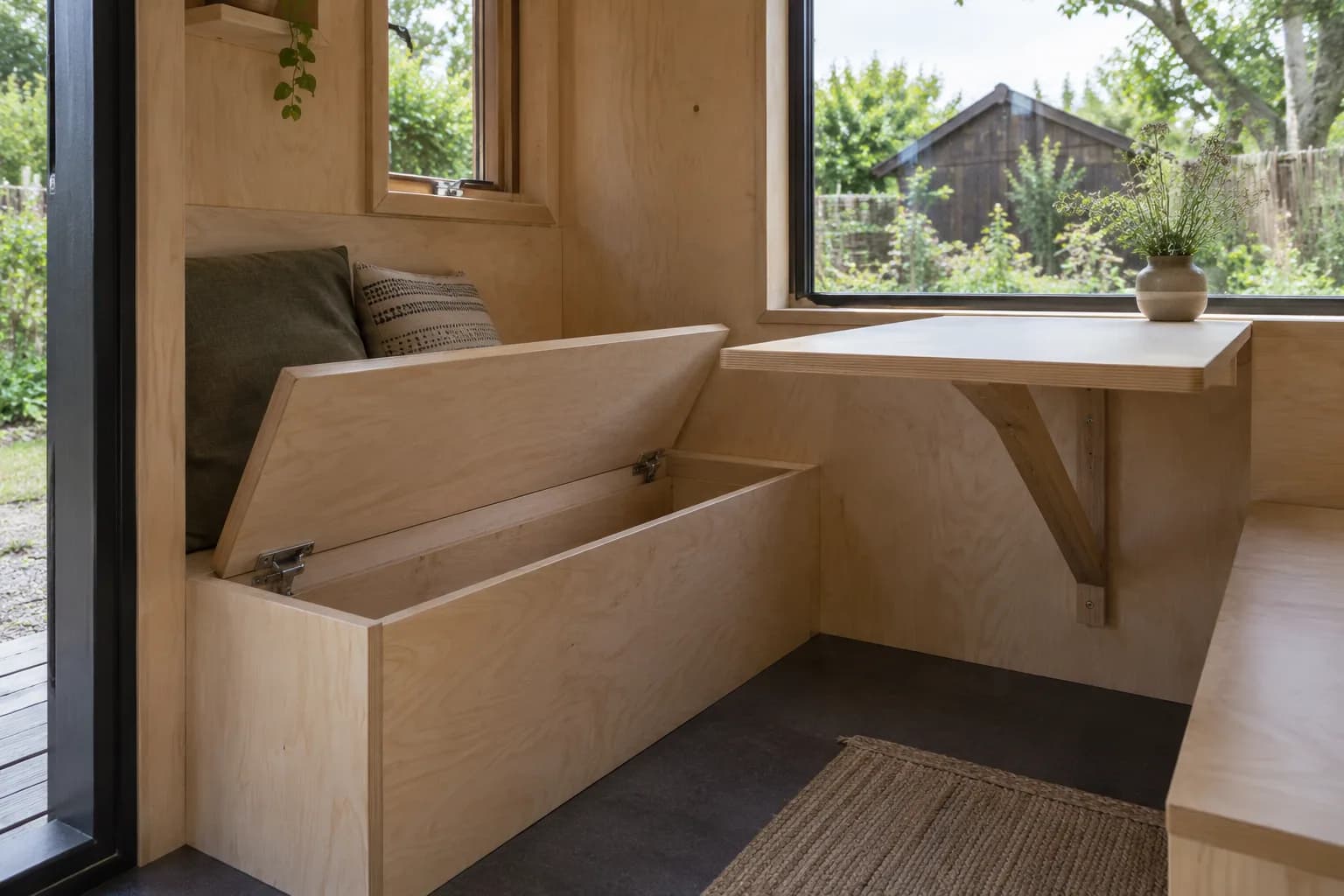 Multiplex zitbank met open opbergruimte en wandtafel met houten steun in een compact tiny house.