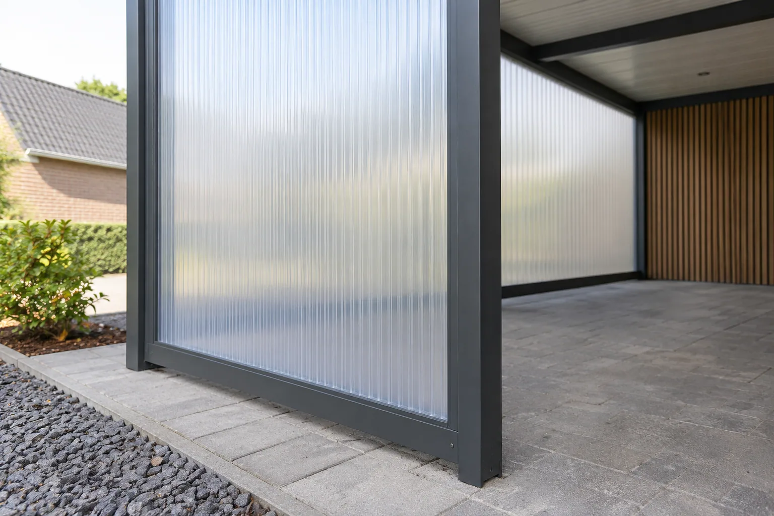 Lichtdoorlatende polycarbonaat zijwand in een antraciet aluminium frame boven de carportbestrating