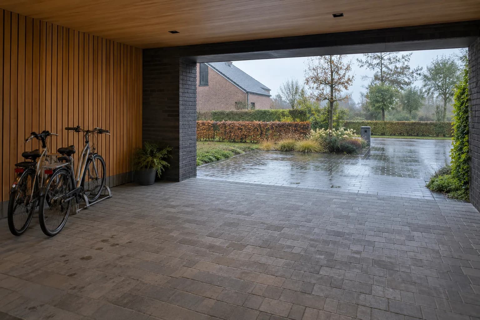 Fietsen staan droog onder een carport met houten zijwand en open toegang naar de natte oprit