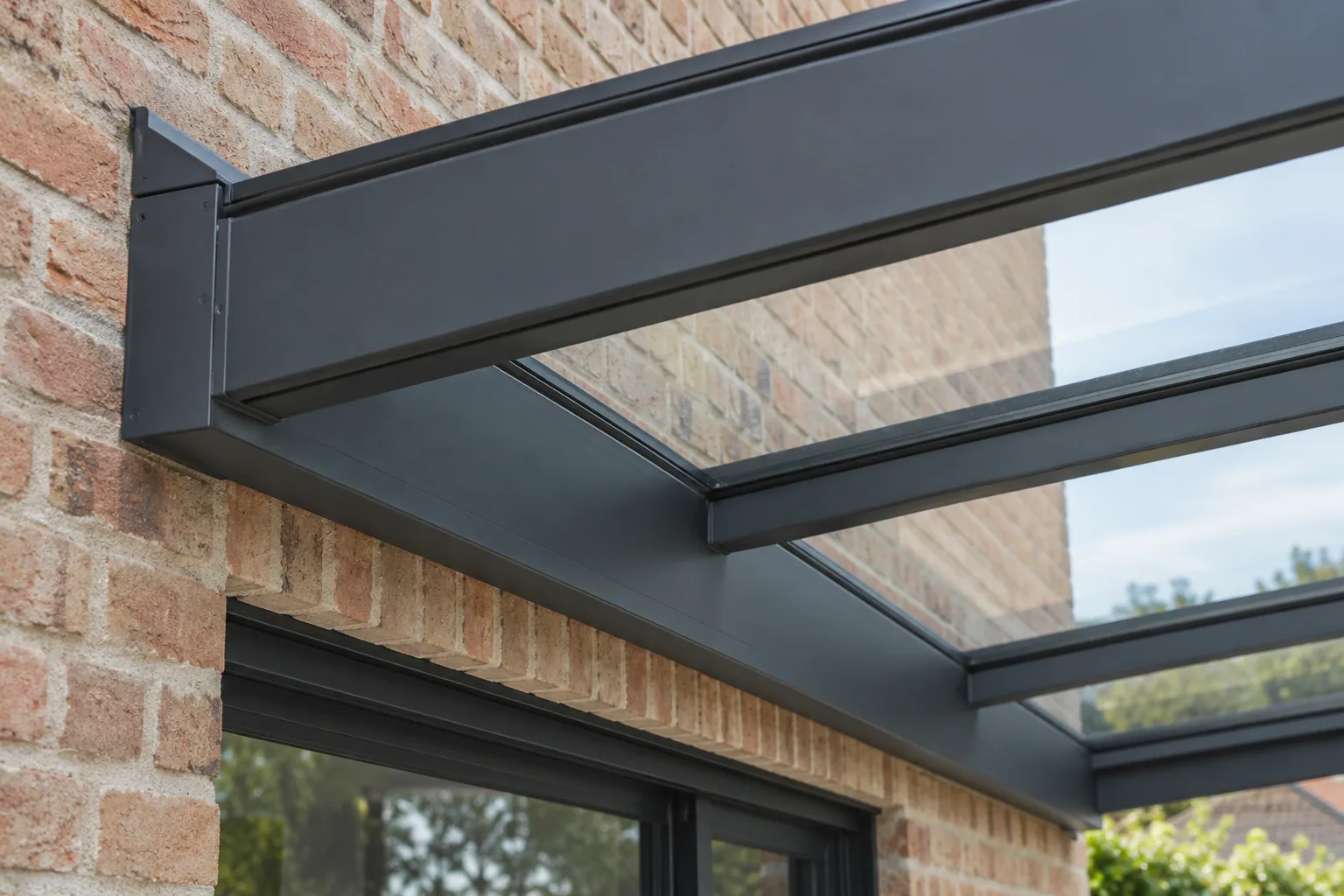 Donkere aluminium dakliggers en glasplaten van een terrasoverkapping bij de aansluiting op een bakstenen gevel