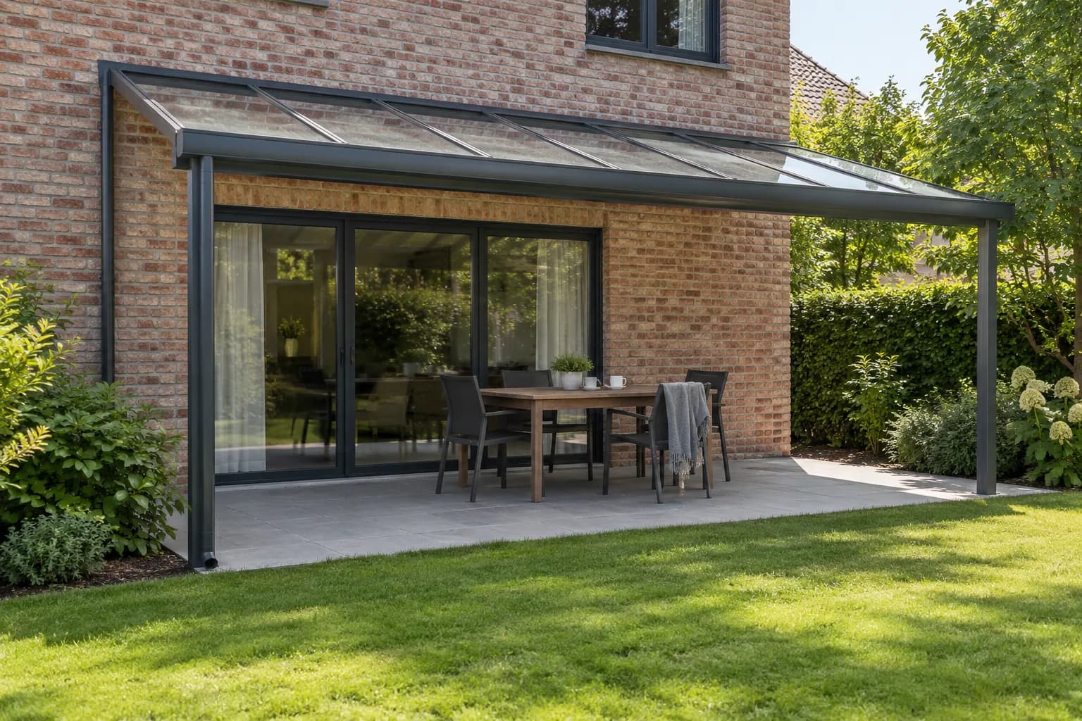 Eettafel onder een glazen terrasoverkapping met aluminium staanders, dakgoot en afvoer naast de woning