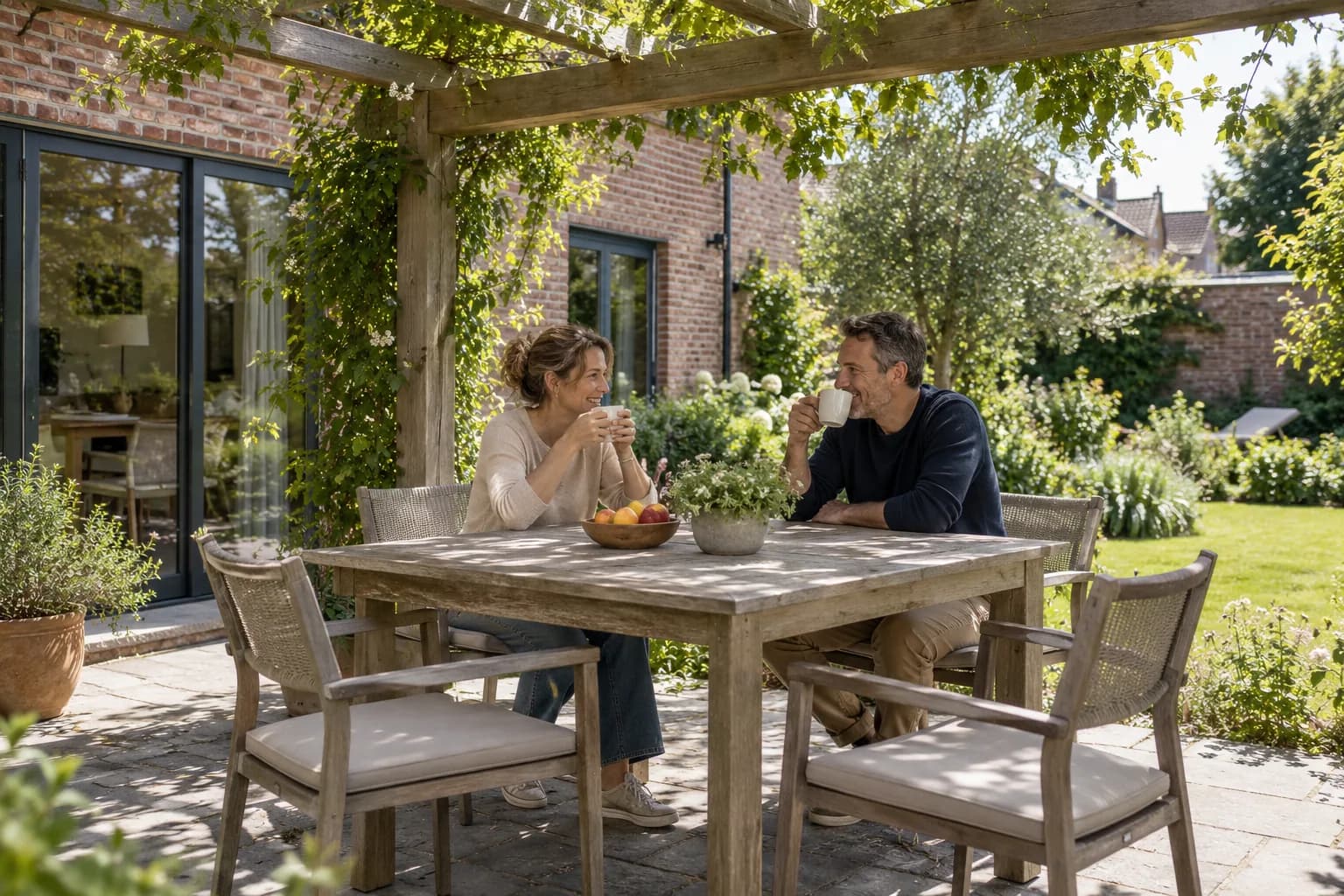 Twee bewoners drinken koffie onder een houten pergola met klimplanten op hun terras.
