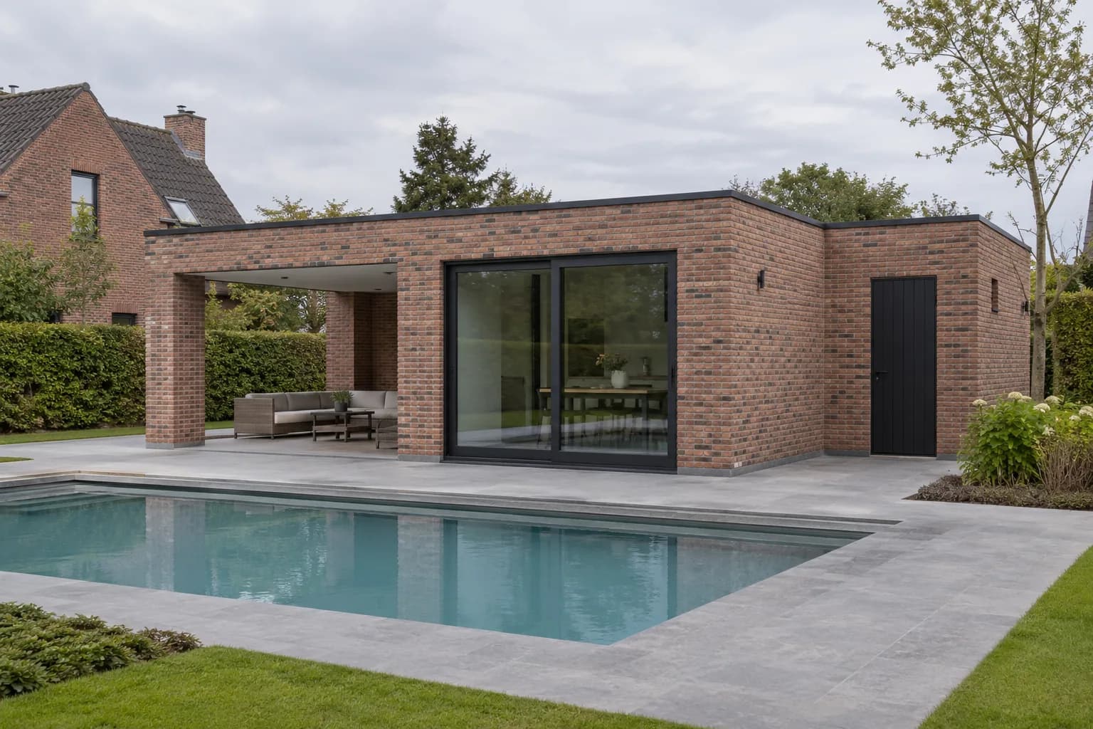 Gemetst poolhouse met plat dak, glazen schuifpui en overdekte zithoek op bakstenen pijlers