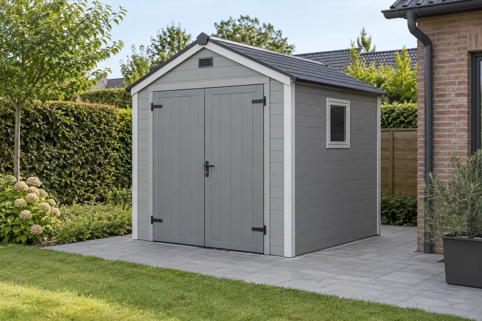 Kunststof tuinhuis met grijze panelen, dubbele deuren en een zadeldak in een tuin.