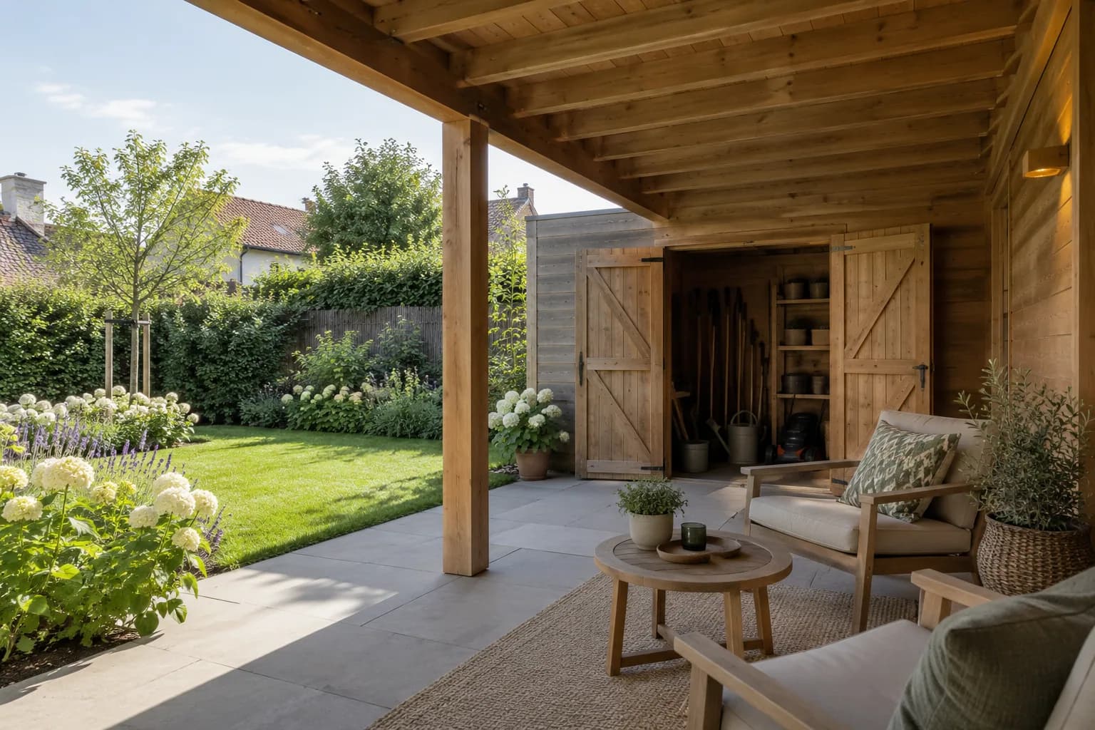 Overdekt terras met zitstoelen naast een houten tuinberging met open deuren.
