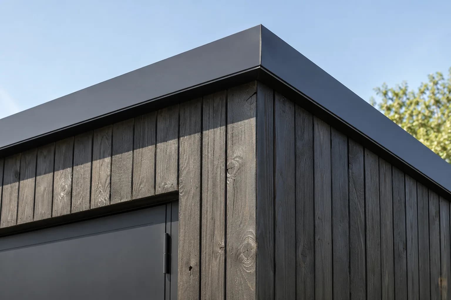Detail van verticale zwarte gevelplanken en de dakrand van een modern tuinhuis.