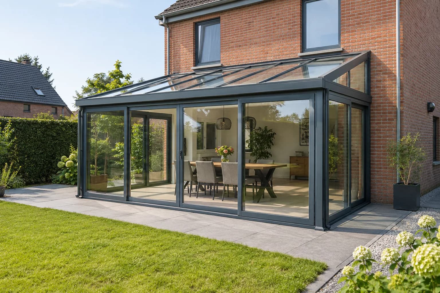 Glazen veranda met aluminium profielen tegen de achtergevel van een bakstenen woning